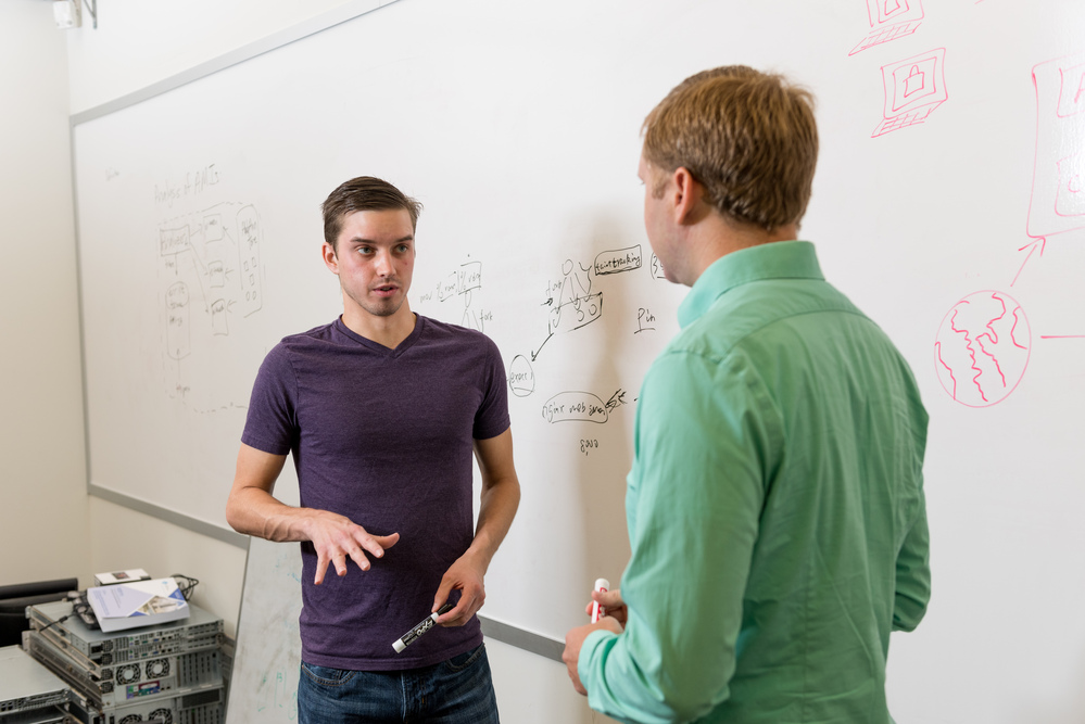 two men working together infront of a large white board