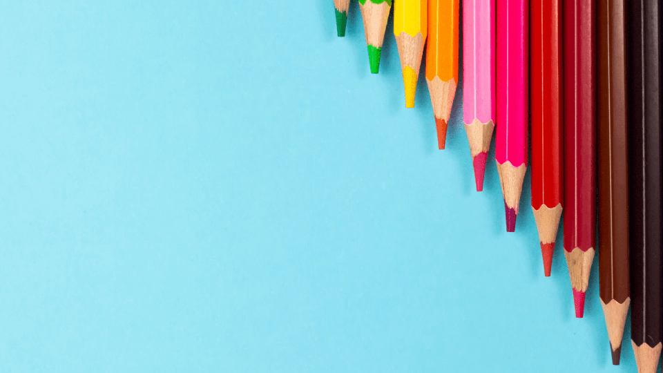 Colored pencils arranged diagonally against a blue background, with sharpened tips pointing inward to create a gradient of vibrant colors.