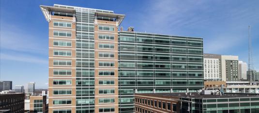 Modern glass and brick office building in an urban district, with surrounding mid-rise buildings and a clear sky.