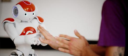 Humanoid robot interacts with a person’s outstretched hands, demonstrating human-robot collaboration and AI research.