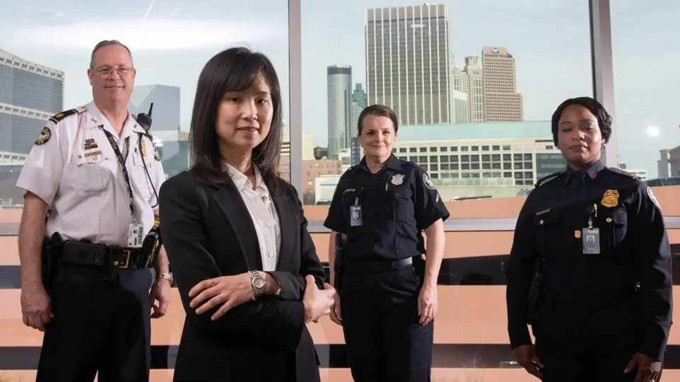 Four public safety and community professionals stand in an office with large windows overlooking a downtown skyline, with one person in business attire positioned in the foreground.