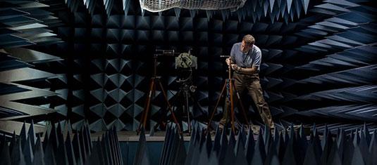 Researcher adjusts equipment inside an anechoic chamber lined with sound-absorbing panels for testing and measurements.