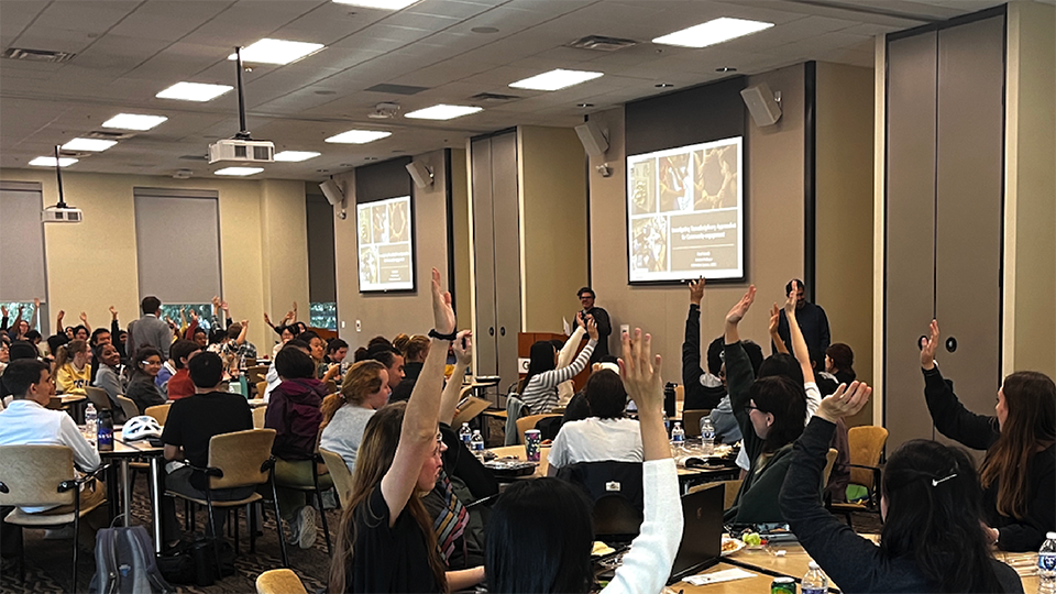Classroom audience raises hands during an interactive presentation in a large lecture and meeting space.