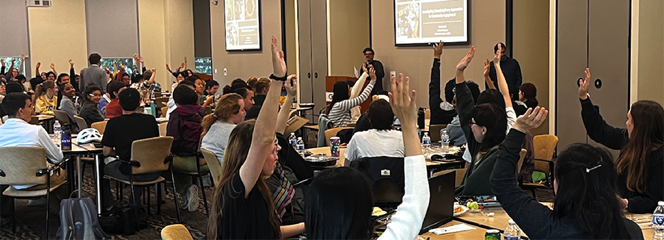 Classroom audience raises hands during an interactive presentation in a large lecture and meeting space.