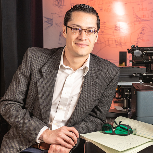 Dr. Francisco Robles in a suit sits next to table with computer, notebook with glasses, and devices on it.