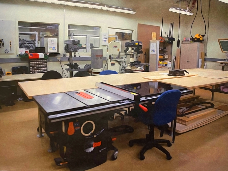 Workshop with large tables, a table saw, drill presses, and tools, arranged for woodworking and prototyping activities.