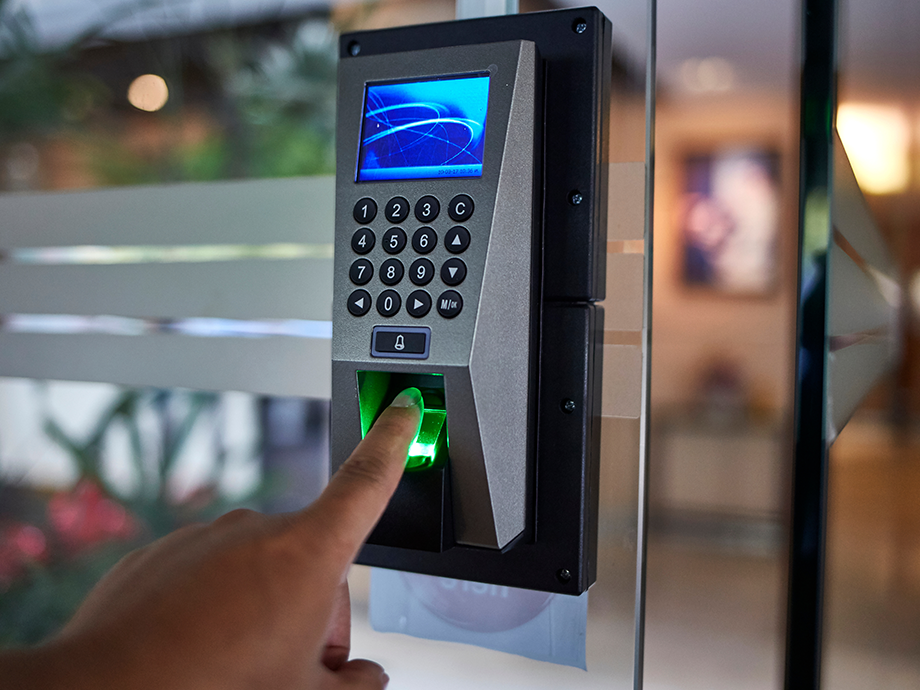 Close-up of a hand pressing a fingerprint scanner on a secure keypad entry system mounted on a glass door.