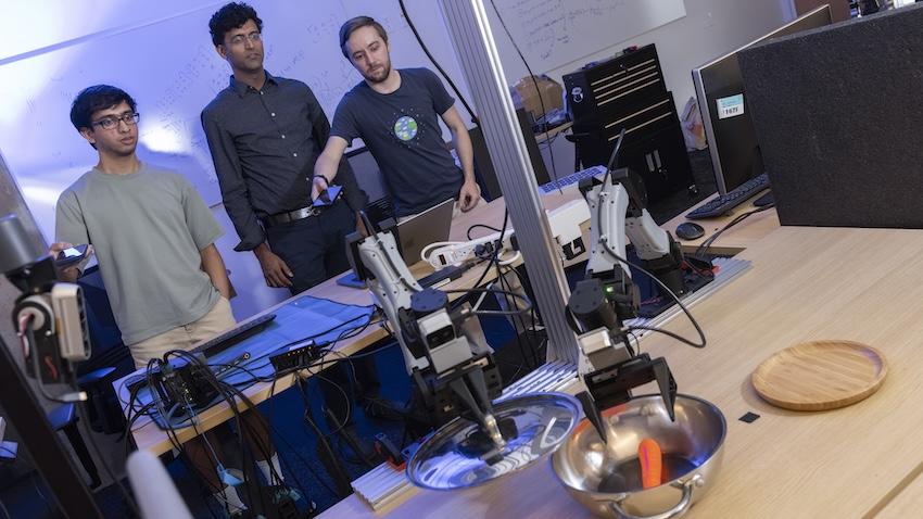 Three men use their phones to control a robot arm