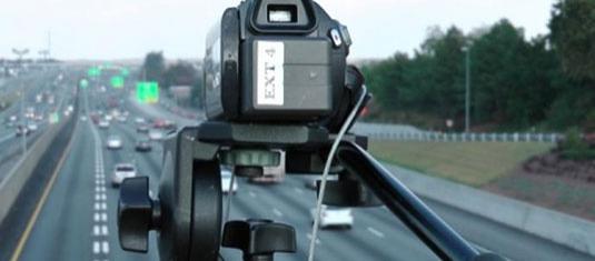 Traffic monitoring camera mounted above a highway, capturing vehicle flow across multiple lanes of traffic.