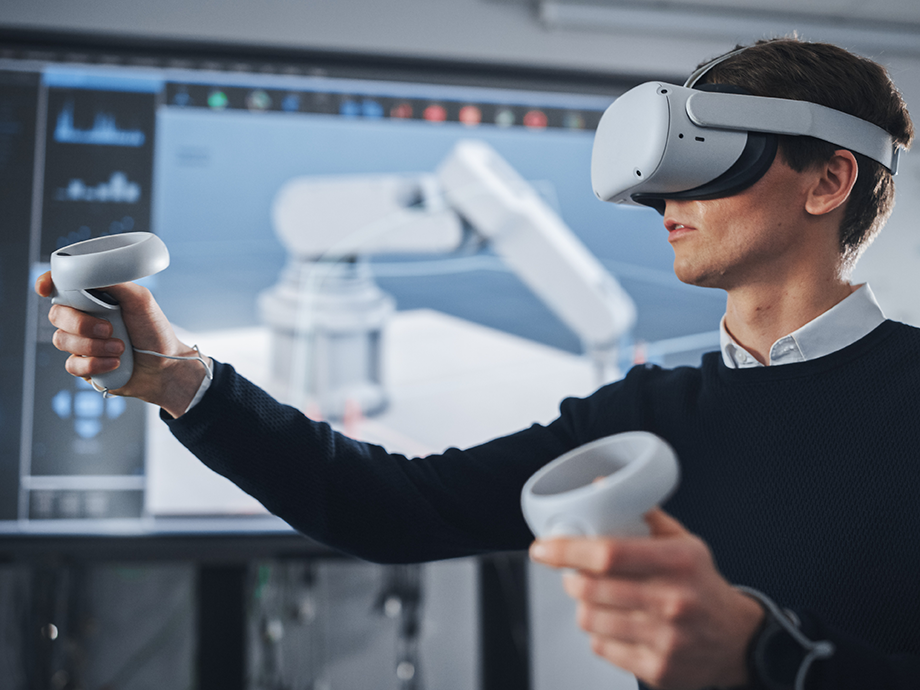 Person wearing a VR headset uses handheld controllers while interacting with a virtual interface displayed on a screen behind them.
